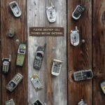 Collection of vintage cell phones attached to a rustic wooden wall with a humorous sign.