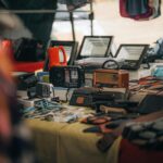 A tabletop display of vintage radios, gadgets, and leather goods at an outdoor flea market.